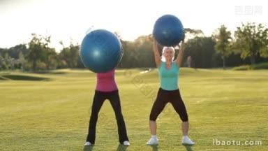 美丽的运动适合的高级妇女在运动服蹲蓝色健身球在绿色的领域在日落微笑成人